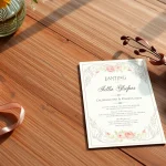 Elegant invitation card showcasing floral patterns and ribbons on a rustic wooden table.